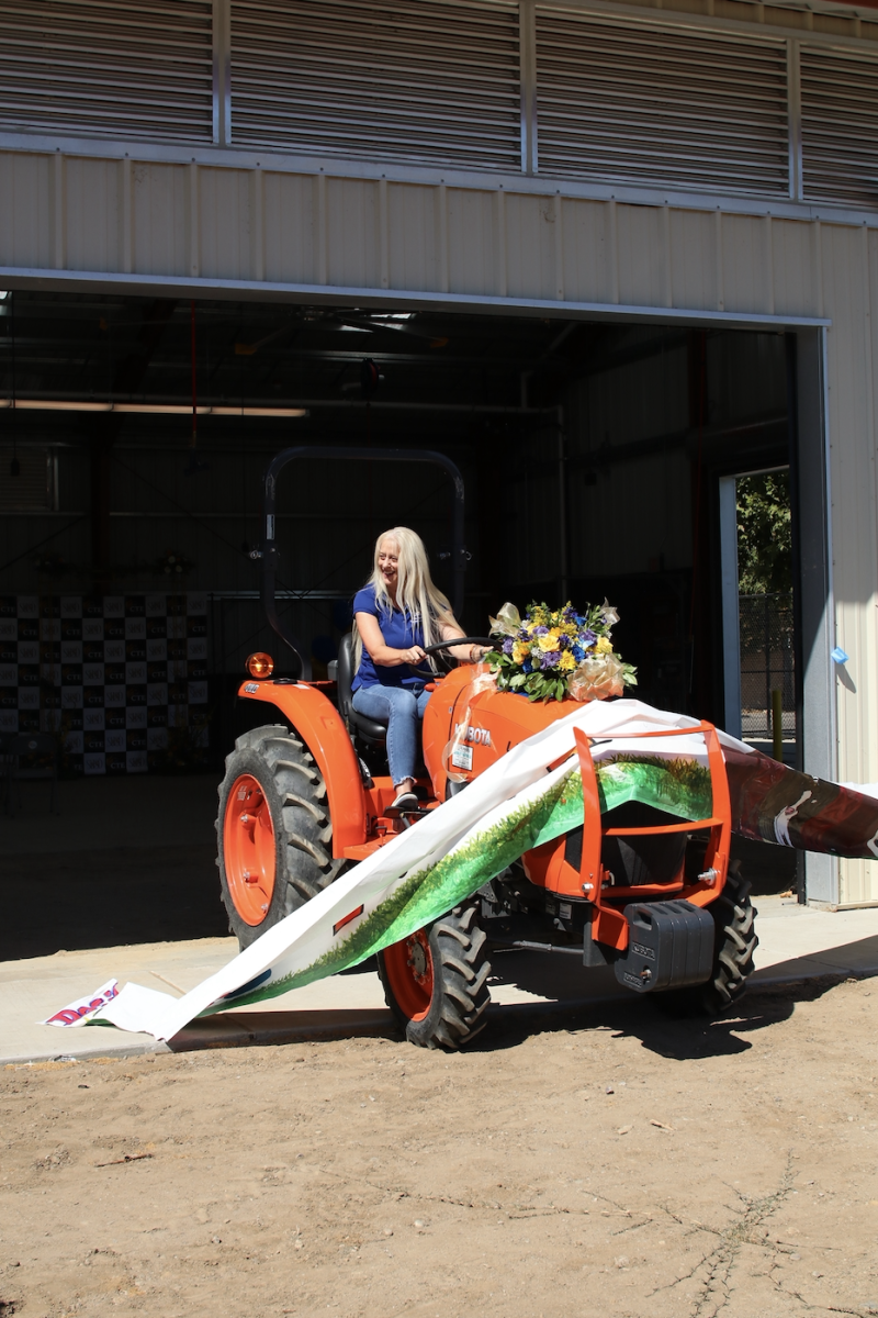 Superintendent Dr. Michelle Rodriguez drives a tractor through the banner that was closing off the front of the barn. The banner was made by Stagg's graphic design class.